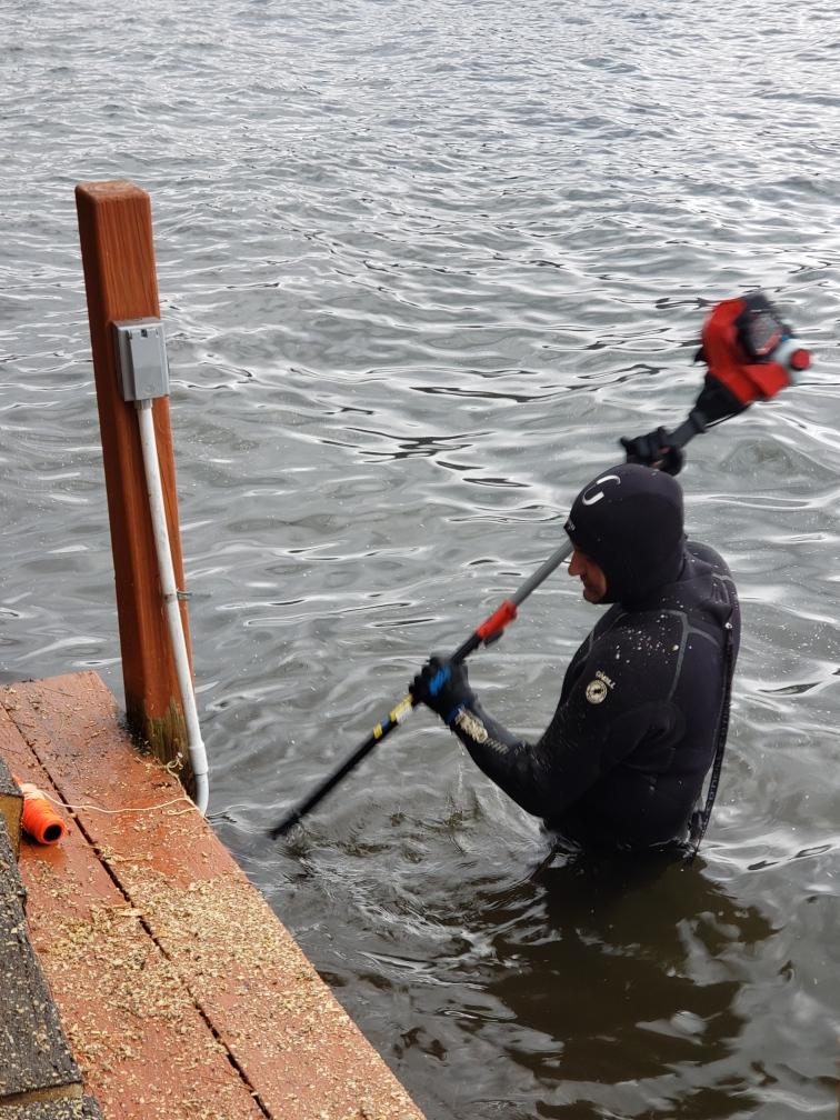 Diver driving a dock piling with a hydraulic tool in cold water