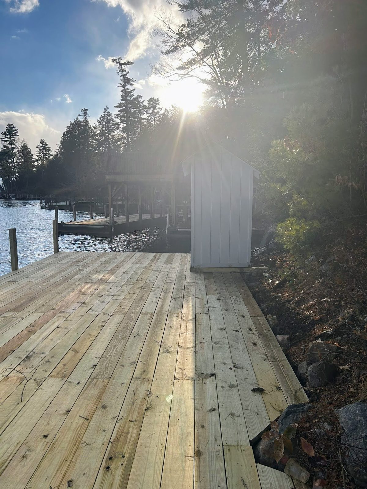 Dock with sun flare through Adirondack pines on Lake George