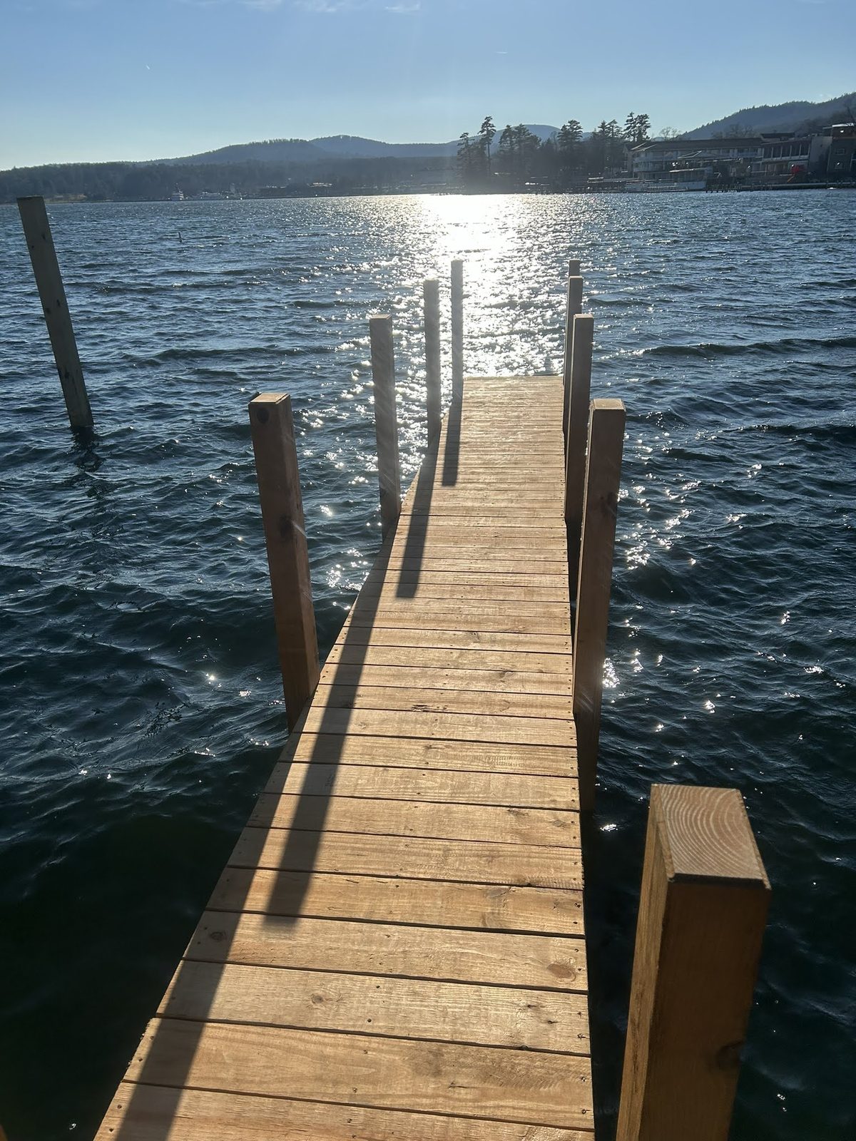 Cedar dock reaching into Lake George at sunrise with the Adirondack shoreline beyond